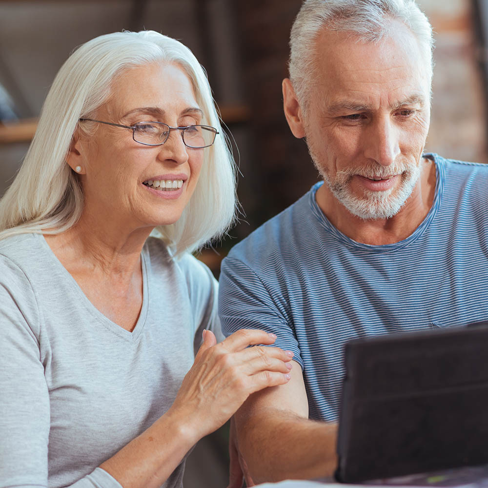 Delighted retired couple using tablet at home